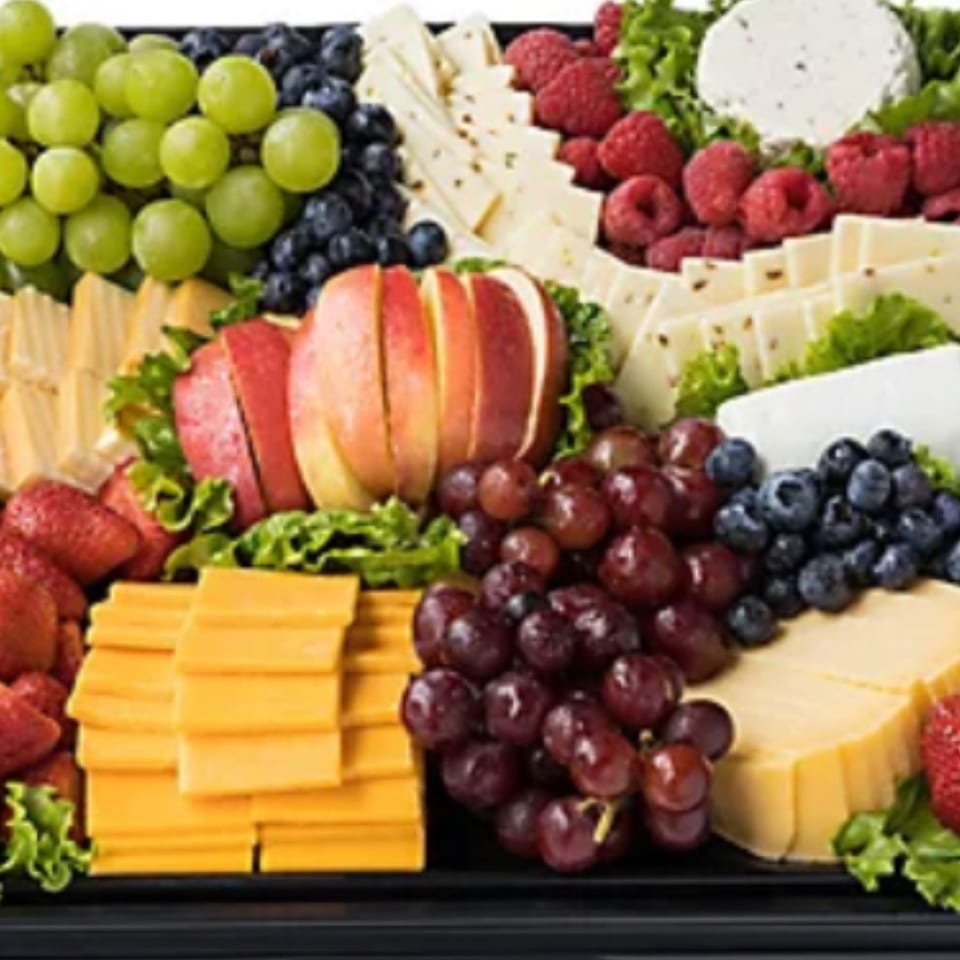 A large platter filled with various cheeses, green and red grapes, blueberries, raspberries, strawberries, and sliced apples.