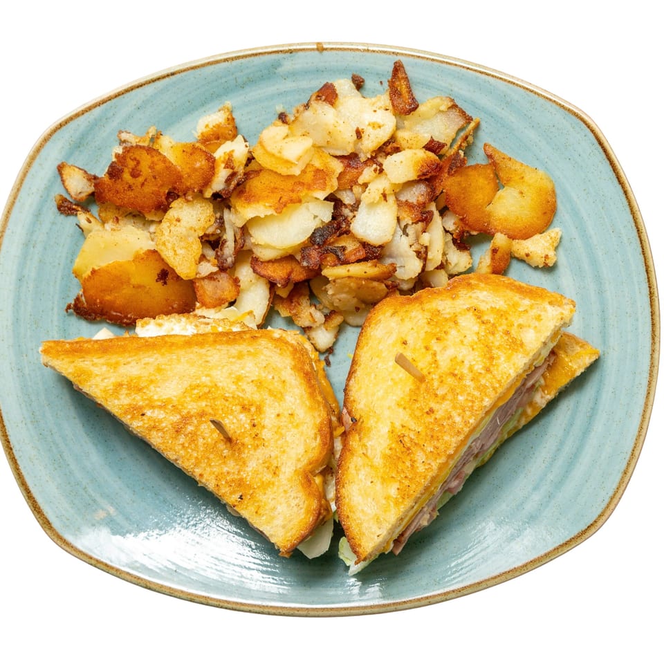 Grilled sandwich halves with cheese and meat, served with a side of crispy home fries on a blue plate.