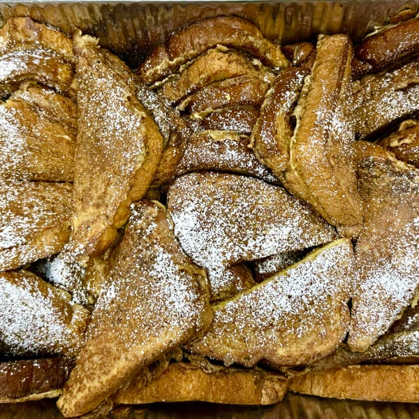 Golden brown French toast triangles, generously dusted with powdered sugar, in a large serving pan.