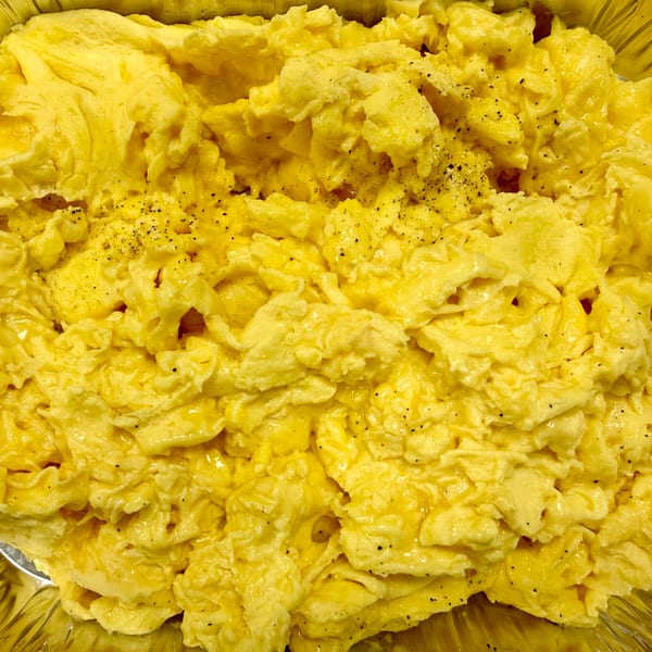 Close-up of fluffy scrambled eggs seasoned with black pepper, served in a foil pan.