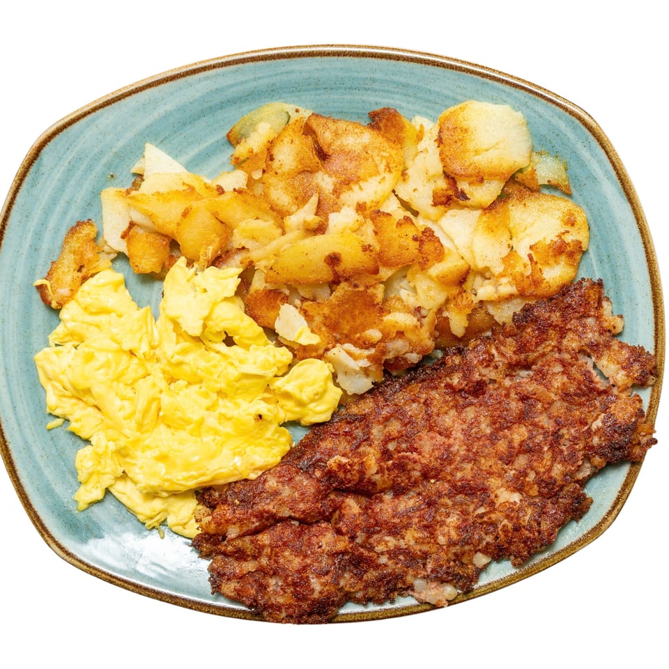 A breakfast plate with scrambled eggs, crispy home fries, and a large patty of corned beef hash.