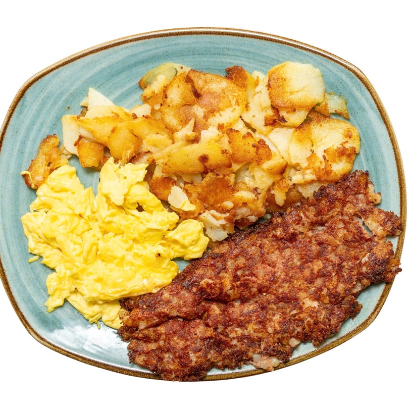 A breakfast plate with scrambled eggs, crispy home fries, and a large patty of corned beef hash.