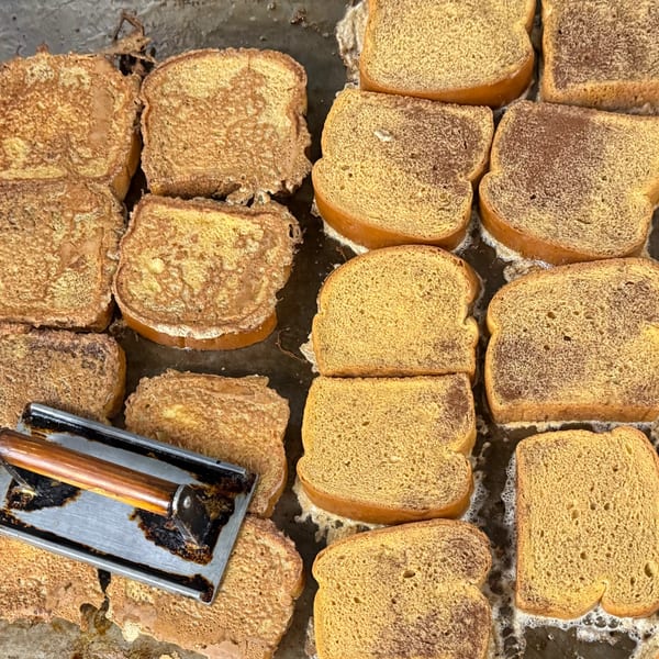 Slices of French toast cooking on a griddle, with a metal press resting on one slice.