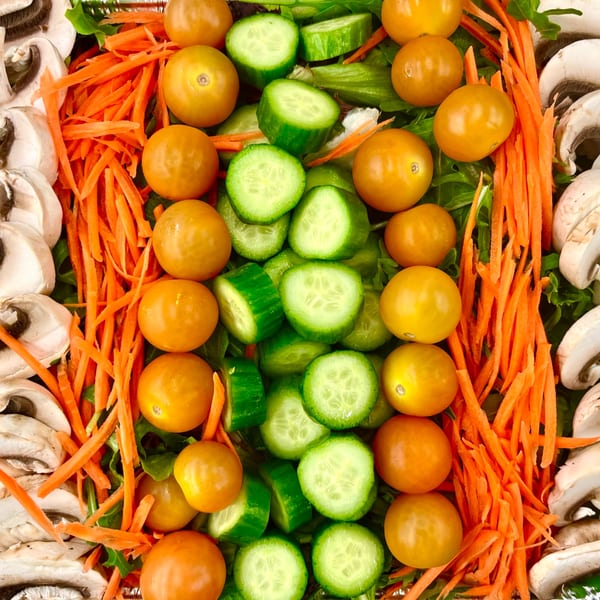 Overhead view of a salad with rows of mushrooms, shredded carrots, cherry tomatoes, and cucumber slices.
