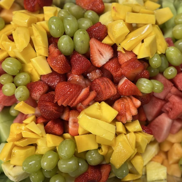 Close-up of a vibrant fruit salad with diced mango, strawberries, and green grapes.